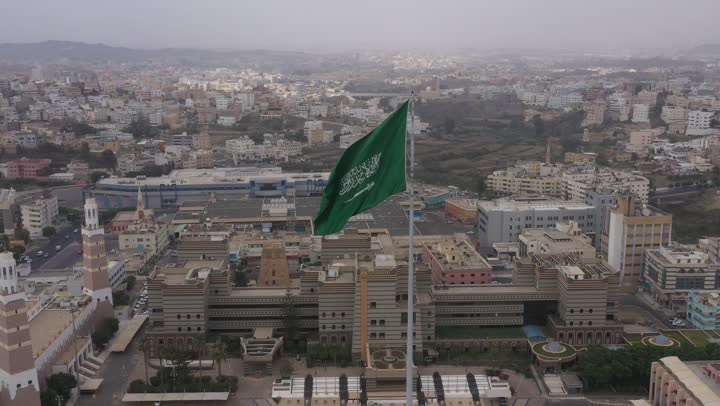 سارية العلم السعودي الأخضر المرفرف في الهواء في دوار الملك فيصل، الفخر والاعتزاز بالانتماء الى الوطن, المعالم المشهورة في مدينة أبها بمنطقة عسير جنوب غرب المملكة