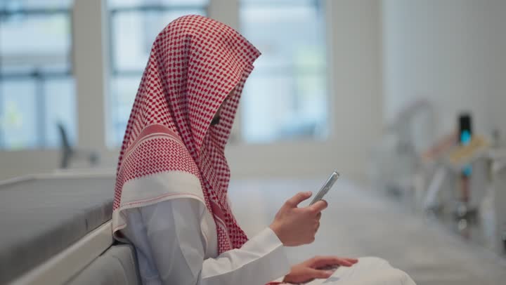 قراءة القران الكريم من الهاتف المحمول، استخدام جهاز تقني حديث ومتطور،  رجل عربي خليجي سعودي يرتدي الثوب التقليدي والشماغ يسجد داخل المسجد، العبادة و التقرب الى الله، التعبد في بيوت الله