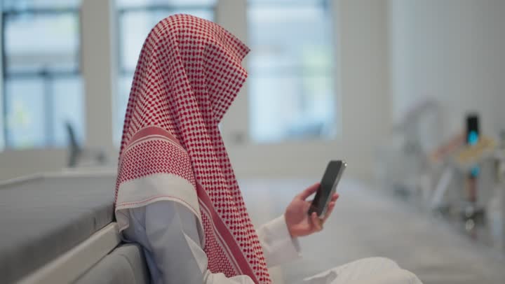 قراءة القران الكريم من الهاتف المحمول، استخدام جهاز تقني حديث ومتطور،  رجل عربي خليجي سعودي يرتدي الثوب التقليدي والشماغ يسجد داخل المسجد، العبادة و التقرب الى الله، التعبد في بيوت الله