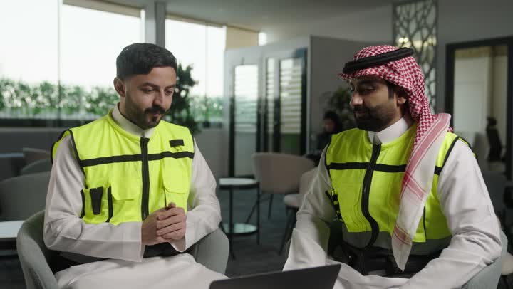 Reviewing new architectural designs on a laptop, an Arab Saudi Gulf architect wearing work attire uses a laptop alongside a colleague, overseeing the electronic application of architectural projects and plans in construction, integrating work with technology and innovation.