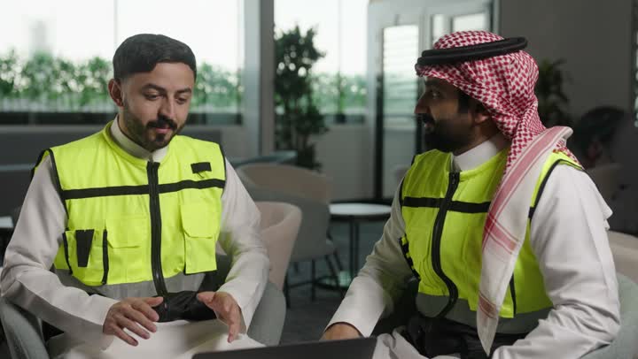 الاطلاع على تصاميم هندسية جديدة على جهاز الحاسوب المحمول، مهندس معماري عربي سعودي خليجي يرتدي اللباس الخاص بالعمل يستخدم اللابتوب برفقة زميله بالعمل ، الاشراف الالكتروني على تطبيق المشاريع و الخطط الهندسيه المعمارية في البناء، دمج العمل مع التقنية و التكنولوجيا