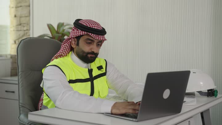 استخدام الادوات الهندسية ، الاطلاع على تصاميم هندسية جديدة على جهاز الحاسوب المحمول، مهندس معماري عربي سعودي خليجي يرتدي اللباس الخاص بالعمل يستخدم اللابتوب برفقة زميله بالعمل ، الاشراف الالكتروني على تطبيق المشاريع و الخطط الهندسيه المعمارية في البناء، دمج العمل مع التقنية و التكنولوجيا