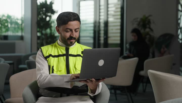 الاشراف الالكتروني على تطبيق المشاريع و الخطط الهندسيه المعمارية في البناء،الاطلاع على تصاميم هندسية جديدة على جهاز الحاسوب المحمول، مهندس معماري عربي سعودي خليجي يرتدي اللباس الخاص بالعمل يستخدم اللابتوب  ،  دمج العمل مع التقنية و التكنولوجيا