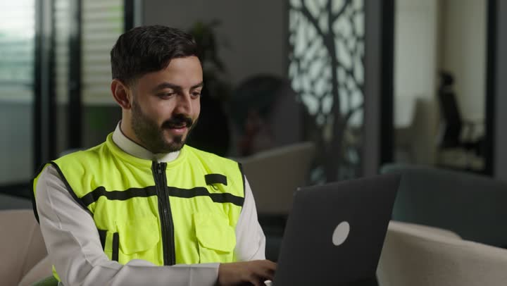 Electronic supervision of the implementation of architectural engineering projects and plans in construction, reviewing new engineering designs on a laptop, an Arab Saudi Gulf architect wearing work attire using a laptop, integrating work with technology and technology.