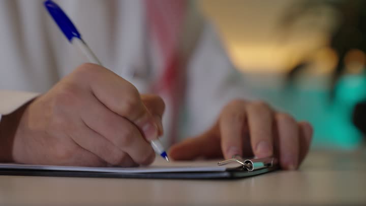 إيماءات الاندماج والتركيز، العمل على الحاسوب المحمول داخل المكتب، مهنة ووظيفة ادارية مكتبية، إدارة شؤون الأعمال عبر جهاز تقني حديث ومتطور، موظف عربي خليجي سعودي يرتدي الثوب والشماغ التقليدي يقوم باستخدام الحاسوب المحمول وتدوين الملاحظاات ، الشركات والمكاتب الهندسية في السعودية