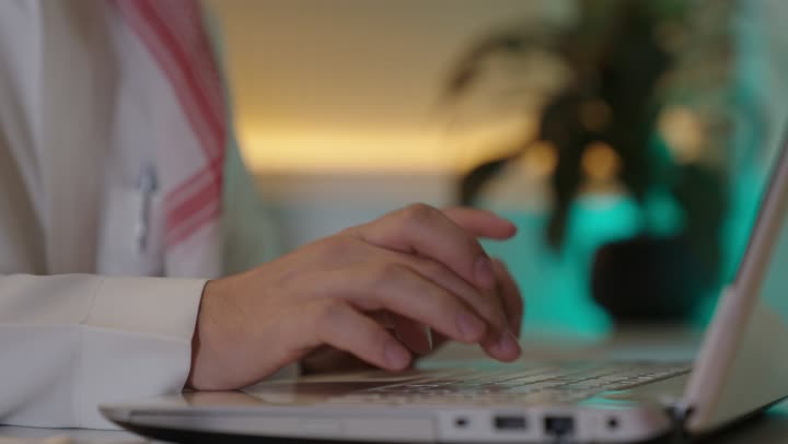 إيماءات الاندماج والتركيز، العمل على الحاسوب المحمول داخل المكتب، مهنة ووظيفة ادارية مكتبية، إدارة شؤون الأعمال عبر جهاز تقني حديث ومتطور، موظف عربي خليجي سعودي يرتدي الثوب والشماغ التقليدي يقوم باستخدام الحاسوب المحمول وتدوين الملاحظاات ، الشركات والمكاتب الهندسية في السعودية