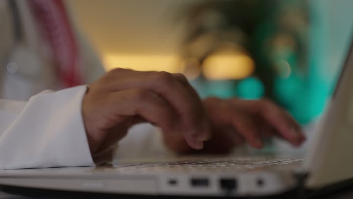 العمل على الحاسوب المحمول داخل المكتب، إيماءات الاندماج والتركيز، مهنة ووظيفة ادارية مكتبية، إدارة شؤون الأعمال عبر جهاز تقني حديث ومتطور، موظف عربي خليجي سعودي يرتدي الثوب والشماغ التقليدي يقوم باستخدام الحاسوب المحمول وتدوين الملاحظاات ، الشركات والمكاتب الهندسية في السعودية