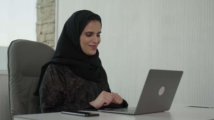 إدارة شؤون الأعمال عبر جهاز تقني حديث ومتطور،مهنة ووظيفة ادارية مكتبية،  إيماءات الاندماج والتركيز، العمل على الحاسوب المحمول داخل المكتب،موظفة عربيه خليجيه سعوديه يرتدي العباءه والحجاب  تقوم باستخدام الحاسوب المحمول وتدوين الملاحظاات ، الشركات والمكاتب الهندسية في السعودية