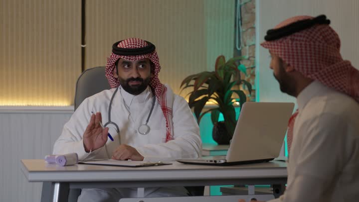 Providing medical consultations and health services, an Arab Gulf Saudi doctor wearing a medical coat and stethoscope, is providing medical care to the patient, the concept of medicine and healthcare.