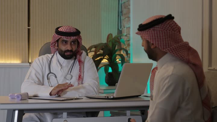 تقديم الاستشارات الطبية والخدمات الصحية، طبيب عربي خليجي سعودي يرتدي المعطف الطبي و السماعة الطبية ،يقوم بتقديم الرعاية الطبية للمريض  , مفهوم الطب والرعاية الصحية