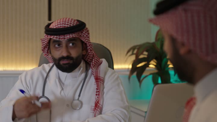 تقديم الاستشارات الطبية والخدمات الصحية، طبيب عربي خليجي سعودي يرتدي المعطف الطبي و السماعة الطبية ،يقوم بتقديم الرعاية الطبية للمريض  , مفهوم الطب والرعاية الصحية