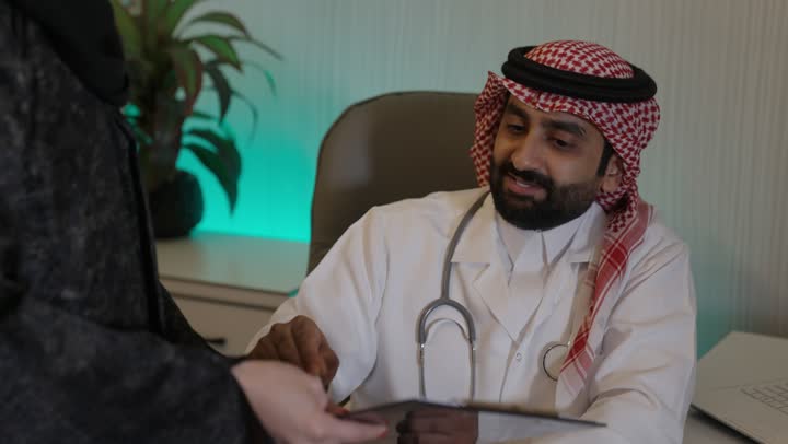 مفهوم الطب والرعاية الصحية ، طبيب تقديم الاستشارات الطبية والخدمات الصحية، طبيب عربي خليجي سعودي يرتدي المعطف الطبي و السماعة الطبية ،يقوم بتقديم الرعاية الطبية للمريضه