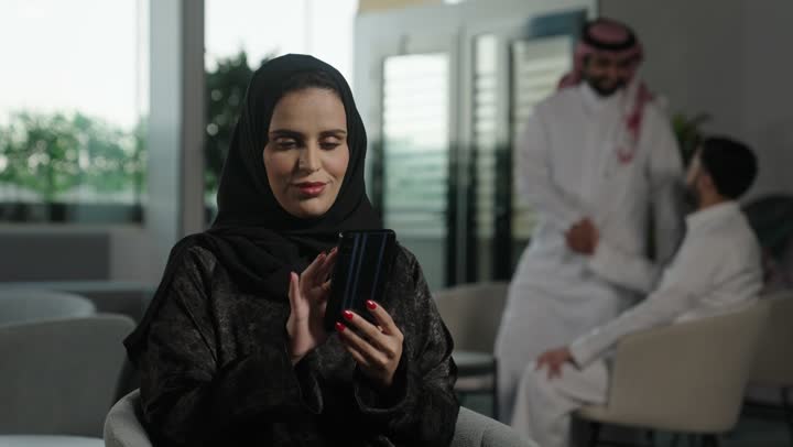 Communicating with family and friends via mobile, chatting online, an Arab Gulf Saudi woman wearing an abaya and hijab holding a mobile phone, using modern and advanced devices, browsing social media.