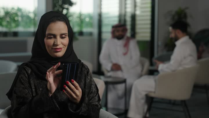 التواصل مع الأهل والأصدقاء عبر الجوال، الدردشة عبر الانترنت, سيدة عربية خليجية سعودية ترتدي العباءة والحجاب تحمل بيدها هاتف محمول , استخدام الأجهزة الحديثة والمتطورة، تصفح وسائل التواصل الاجتماعي.