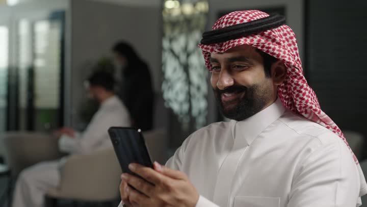 الدردشة عبر الانترنت, التواصل مع الأهل والأصدقاء عبر الجوال، رجل عربي خليجي سعودي يرتدي الزي التقليدي والشماغ يحمل بيده هاتف محمول , استخدام الأجهزة الحديثة والمتطورة، تصفح وسائل التواصل الاجتماعي.