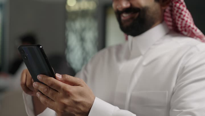 الدردشة عبر الانترنت, التواصل مع الأهل والأصدقاء عبر الجوال، رجل عربي خليجي سعودي يرتدي الزي التقليدي والشماغ يحمل بيده هاتف محمول , استخدام الأجهزة الحديثة والمتطورة، تصفح وسائل التواصل الاجتماعي.