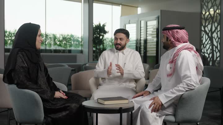 بيئة العمل المريحة في الشركات السعودية، الحوار و النقاش بين الزملاء،  مجموعة من موظفين عربيين خليجيين سعوديين يجلسون  داخل مقر الشركة، تبادل الخبرات والمعلومات لتحقيق الاهداف