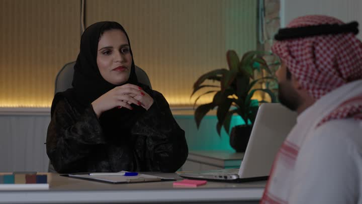 الحوار و النقاش بين الزملاء، بيئة العمل المريحة في الشركات السعودية، تبادل الخبرات والمعلومات لتحقيق الاهداف, موظفان عربيان خليجيان سعوديان يعملان في مكتبهم داخل مقر الشركة، استخدام الحاسب والتقنية في مجال الاعمال