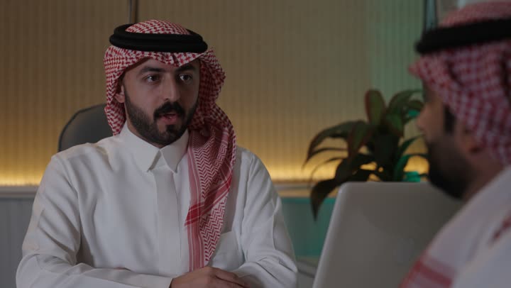 بيئة العمل المريحة في الشركات السعودية، تبادل الخبرات والمعلومات لتحقيق الاهداف, الحوار و النقاش بين الزملاء، موظفان عربيان خليجيان سعوديان يعملان في مكتبهم داخل مقر الشركة