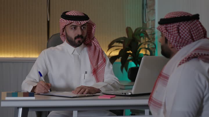 كتابة وتسجيل الملاحظات في مجال الاعمال، الحوار و النقاش بين الزملاء، بيئة العمل المريحة في الشركات السعودية، تبادل الخبرات والمعلومات لتحقيق الاهداف, موظفان عربيان خليجيان سعوديان يعملان في مكتبهم داخل مقر الشركة، استخدام الحاسوب المحمول