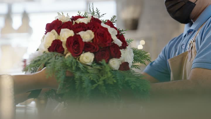 متاجر ومحلات بيع الورود والزهور الطبيعية للأعياد والمناسبات, امرأة عربية خليجية سعودية ترتدي العباءة والحجاب تقوم بشراء باقة ورد احمر طبيعي من البائع , ايماءات تدل على الفرح والسعاده