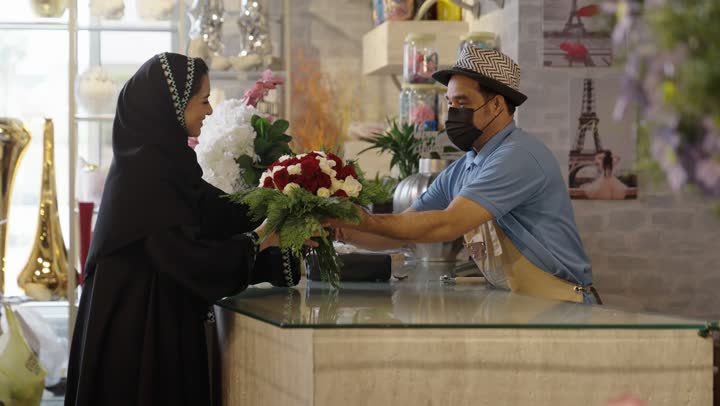 متاجر ومحلات بيع الورود والزهور الطبيعية للأعياد والمناسبات, امرأة عربية خليجية سعودية ترتدي العباءة والحجاب تقوم بشراء باقة ورد احمر طبيعي من البائع , ايماءات تدل على الفرح والسعاده