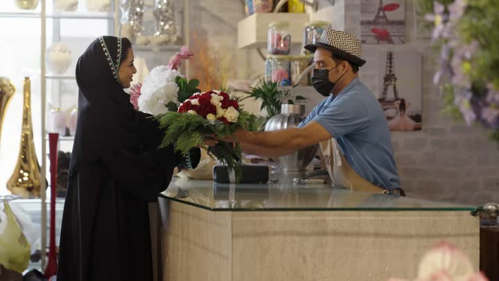 متاجر ومحلات بيع الورود والزهور الطبيعية للأعياد والمناسبات, امرأة عربية خليجية سعودية ترتدي العباءة والحجاب تقوم بشراء باقة ورد احمر طبيعي من البائع , ايماءات تدل على الفرح والسعاده