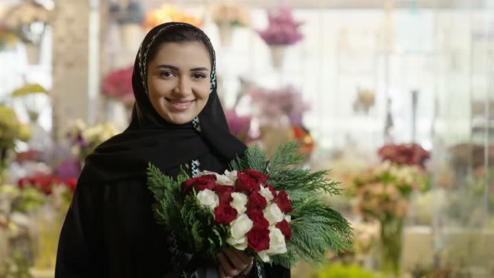 شراء الورود والزهور الطبيعية للأعياد والمناسبات من المحلات والمتاجر, امرأة عربية خليجية سعودية ترتدي العباءة والحجاب تحمل باقة ورد احمر طبيعي بايماءات الفرح والسعاده
