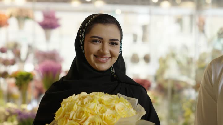 زوجان عربيان خليجيان سعوديان سعيدان يحتفلان بعيد الحب , الزوج يقدم لزوجته باقة ورد , الزوجة تعبر بإيماءات وجه ويدين تدل على الدهشة والفرح , عيد الأم , يوم الفلانتاين , أعياد ومناسبات , عيد الميلاد  .