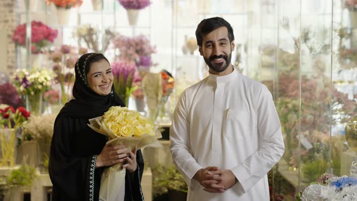 زوجان عربيان خليجيان سعوديان سعيدان يحتفلان بعيد الحب , الزوج يقدم لزوجته باقة ورد , الزوجة تعبر بإيماءات وجه ويدين تدل على الدهشة والفرح , عيد الأم , يوم الفلانتاين , أعياد ومناسبات , عيد الميلاد  .