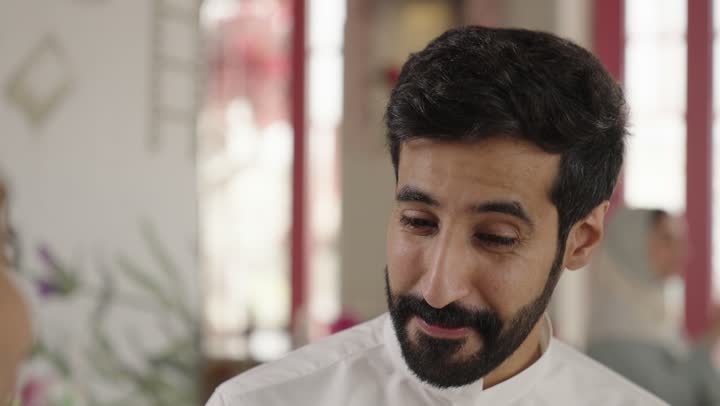 Spending enjoyable time outdoors, entertainment and fun during the holiday, two Arab Gulf men from Saudi Arabia wearing traditional attire sitting in a restaurant with gestures of happiness and joy, sharing hot drinks, coffee, and sweets, exchanging conversations among friends.