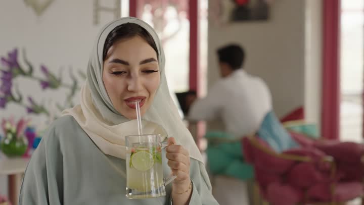 مشاركة المشروبات الساخنة والقهوة والحلويات،التسلية والترفيه في العطلة،قضاء وقت ممتع في الخارج،  صديقتان عربيتان خليجيتان سعوديتان ترتديان العباءه والحجاب تجلسان في المطعم بايماءات السعادة والسرور،  تبادل الاحاديث بين الأصدقاء