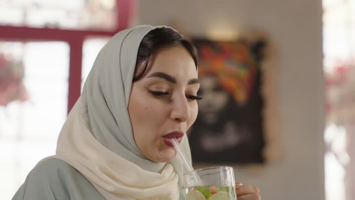 التسلية والترفيه في العطلة، مشاركة المشروبات الساخنة والقهوة والحلويات، قضاء وقت ممتع في الخارج،  صديقتان عربيتان خليجيتان سعوديتان ترتديان العباءه والحجاب تجلسان في المطعم بايماءات السعادة والسرور،  تبادل الاحاديث بين الأصدقاء