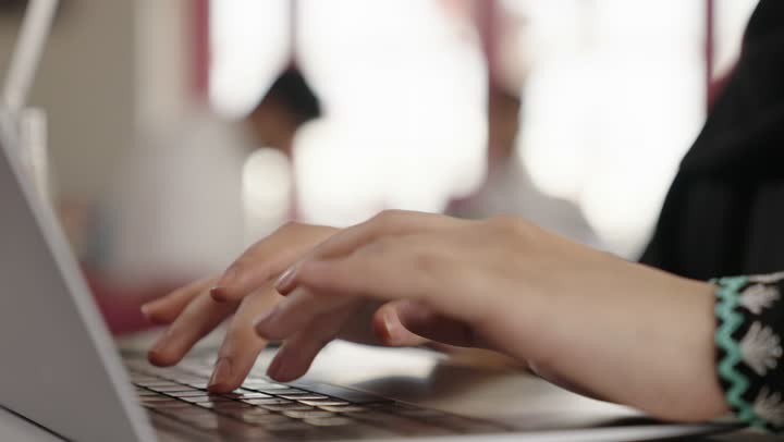 استخدام الأجهزة التقنية الحديثة والمتطورة، ادارة شؤون الاعمال وتنظيمها، تصفح مواقع التواصل الإجتماعي والعمل عن بعد في الكافيه، امراه عربيه خليجيه سعوديه ترتدي العباءه والحجاب تجلس في المطعم وتستخدم  الحاسوب المحمول