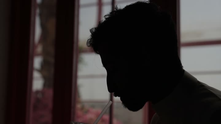 استخدام الأجهزة التقنية الحديثة والمتطورة، ادارة شؤون الاعمال وتنظيمها، تصفح مواقع التواصل الإجتماعي والعمل عن بعد في الكافيه، رجل عربي خليجي سعودي يرتدي الزي التقليدي والشماغ  يجلس في مطعم مظلم  ويستخدم الحاسوب المحمول