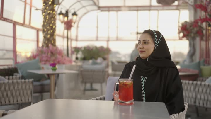 تعابير السعادة والسرور بلمة الرفاق، شرب المشروبات البارده ، مطاعم وكافيهات فى المملكة العربية السعودية ، امراه عربية خليجية سعودية تجلس فى مطعم وتمسك بيها كوب من العصير