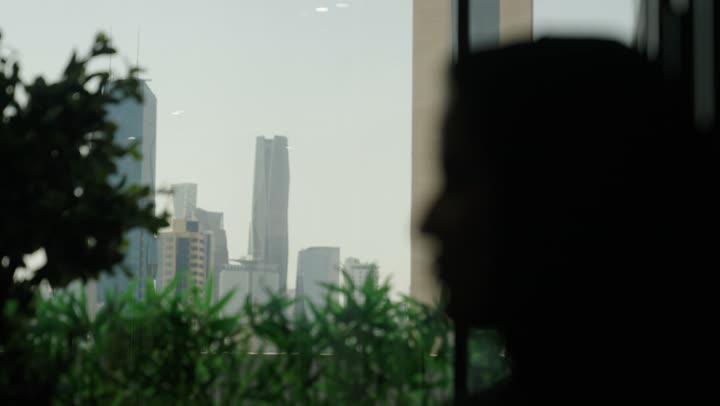 A shadowy image of a Saudi Arabian Gulf man looking through the window at the King Abdullah Financial Towers in Riyadh, admiring the financial commercial center, the growth and urban development in the country, Vision 2030.