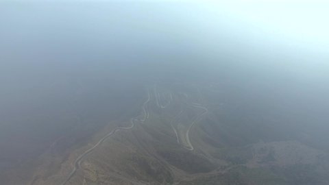 حركة سير السيارات على ممر جبلي ملتوي، المناطق الطبيعية والمعالم التاريخية السياحية في عسير، تصوير درون لطريق عقبة سنانة، الأجواء الضبابية والطبيعة الصحراوية والمرتفعات الجبلية في المملكة العربية السعودية