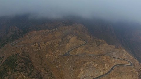 Traffic on a winding mountain pass, natural areas and historical tourist attractions in Asir, drone footage of the Sinana Pass road, foggy weather, desert landscape and mountainous heights in the Kingdom of Saudi Arabia