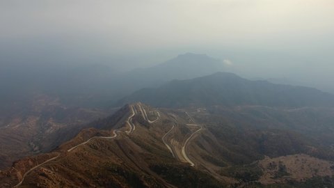 Traffic on a winding mountain pass, natural areas and historical tourist attractions in Asir, drone footage of the Sinana Pass road, foggy weather, desert landscape and mountainous heights in the Kingdom of Saudi Arabia