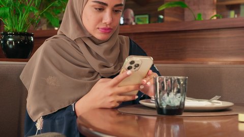 Exchanging messages and chatting with friends online, a close-up shot of an Emirati Gulf Arab woman sitting in a cafe following social media news using her mobile phone, a Saudi woman browsing mobile applications.