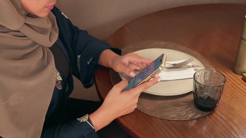 التفاعل مع الأصدقاء من خلال تطبيقات المحادثة، تصوير مقرب لامراة عربيه خليجيه اماراتية تجلس فى احد المقاهي تقوم بمتابعة اخبار وسائل التواصل الاجتماعي باستخدام الجوال،  سيده سعودية تقوم بتصفح تطبيقات الهاتف المحمول