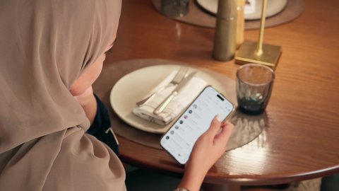 التواصل مع الأصدقاء عبر المحادثات الإلكترونية، تصوير مقرب  لامراة عربيه خليجيه اماراتية تجلس فى احد المقاهي تقوم بمتابعة اخبار وسائل التواصل الاجتماعي باستخدام الجوال،  سيده سعودية تقوم بتصفح تطبيقات الهاتف المحمول