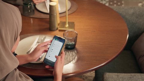 الدردشة والتحدث مع الاصدقاء عبر الانترنت، تصوير مقرب من الخلف لامراة عربيه خليجيه اماراتية تجلس فى احد المقاهي تقوم بمتابعة اخبار وسائل التواصل الاجتماعي باستخدام الجوال،  سيده سعودية تقوم بتصفح تطبيقات الهاتف المحمول