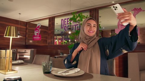 التقاط صور سيلفي تذكارية عبر الجوال, توثيق اللحظات السعيدة, سيده سعودية تقضي اوقات ممتعه في المقهي, امرأة عربية خليجية اماراتية محجبة ترتدي العباءة تحمل الهاتف المحمول تشير بيديها بعلامة النصر