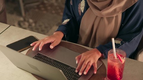 الكتابة على لوحة المفاتيح، استخدام الأجهزة التقنية الحديثة والمتطورة لانجاز المشاريع في الكافيه، العمل عن بعد،  تصوير مقرب ليد امراة عربيه خليجيه اماراتية ترتدي العباءة تستخدم الحاسب المحمول ،الاستمتاع بتناول المشروبات المنعشة