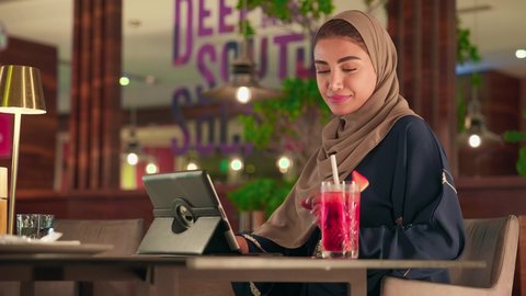 استعمال الجهاز اللوحي في إنجاز العمل الدردشة مع الأهل والأصدقاء، امراة عربيه خليجيه اماراتية  تجلس فى الكافية تقوم باستخدام جهاز التابلت، تصفح مواقع التواصل الاجتماعي، استخدام تطبيقات وبرامج الأجهزة اللوحية, سيده سعودية تستمع بتناول المشروب المفضل