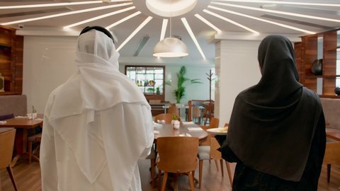 مفهوم الرابطة الزوجية والألفة ، الاستمتاع بتناول وجبة الافطار ، قضاء وقت ممتع في الخارج, تصوير من الخلف لزوجان عربيان خليجيان اماراتيان يرتديان الزي التقليدي يقومان بتناول وجبه الغذاء في احدى المطاعم الاماراتية