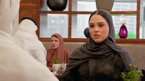 مناقشات أسرية ودية حول يوميات العائلة على المائدة ، قضاء وقت ممتع في الخارج, تصوير مقرب لامراة عربية خليجيه اماراتية محجبه ترتدي العباءة تجلس برفقة زوجها في احدى المطاعم الاماراتية، ايماءات السعادة و السرور