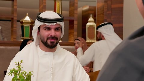 الاستمتاع بتناول وجبة الافطار، حوارات ونقاشات عائلية، قضاء وقت ممتع في الخارج، مفهوم الألفة والمحبة بين أفراد الأسرة, تصوير مقرب لرجل عربي خليجي اماراتي يرتدي الكندورة والغترة يجلس برفقة زوجته في احدى المطعام الاماراتية، ايماءات السعادة و السرور